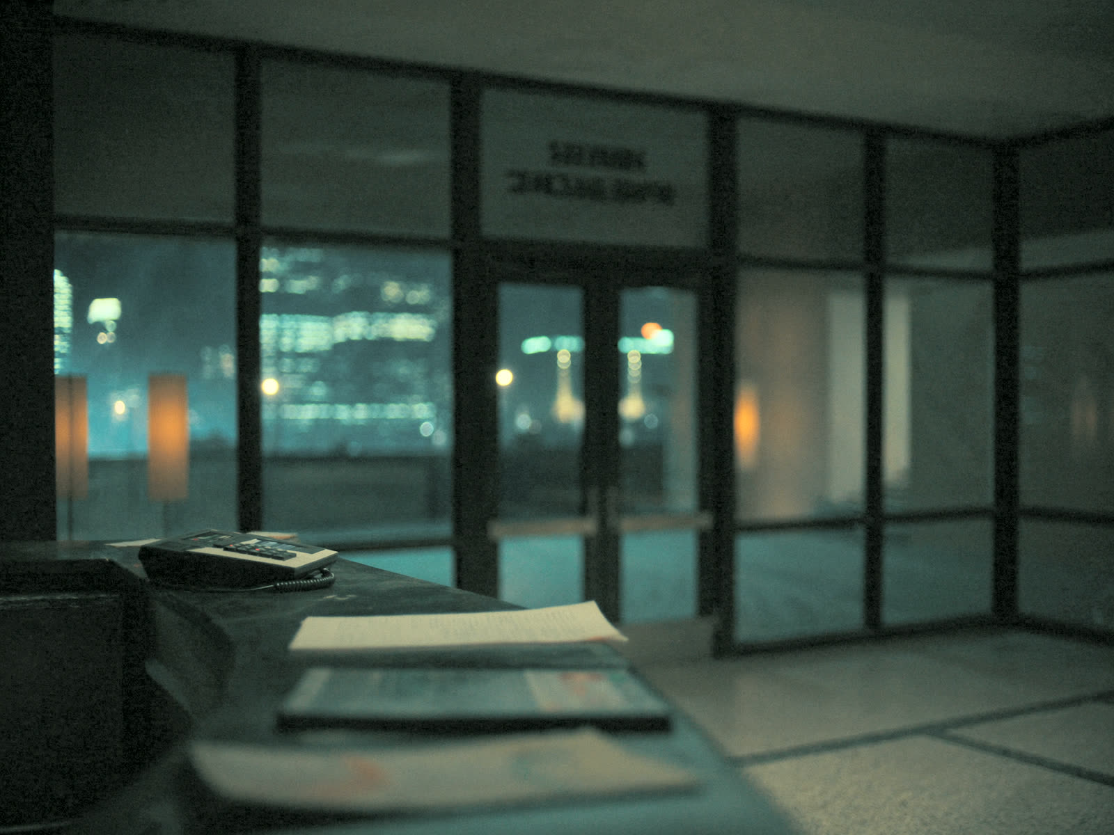 An empty apartment building lobby desk at night with a phone glowing with an incoming call.