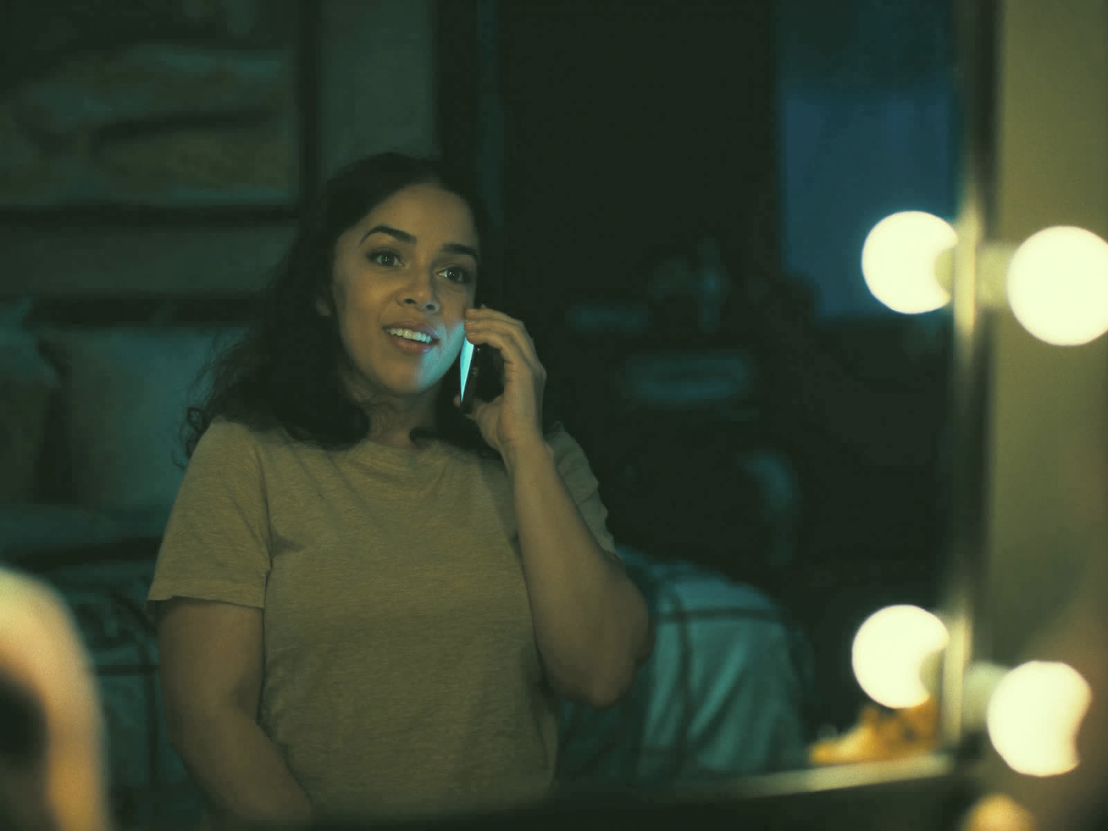 A woman at her vanity mirror smiles on the phone as her hair appointment gets booked.