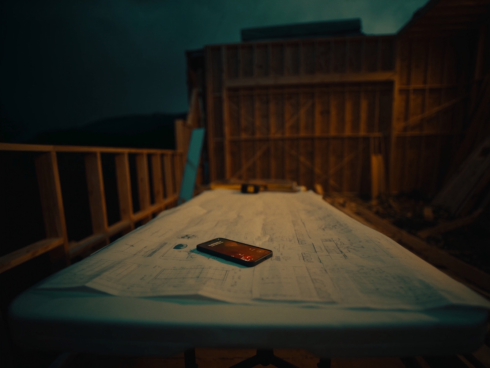 A phone glows with an incoming call on top of blueprints on an empty construction site table at dusk.