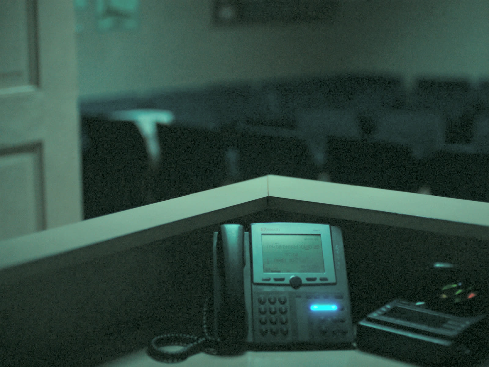 An empty dental office reception desk at night, a phone glowing with an incoming call nobody is there to take.