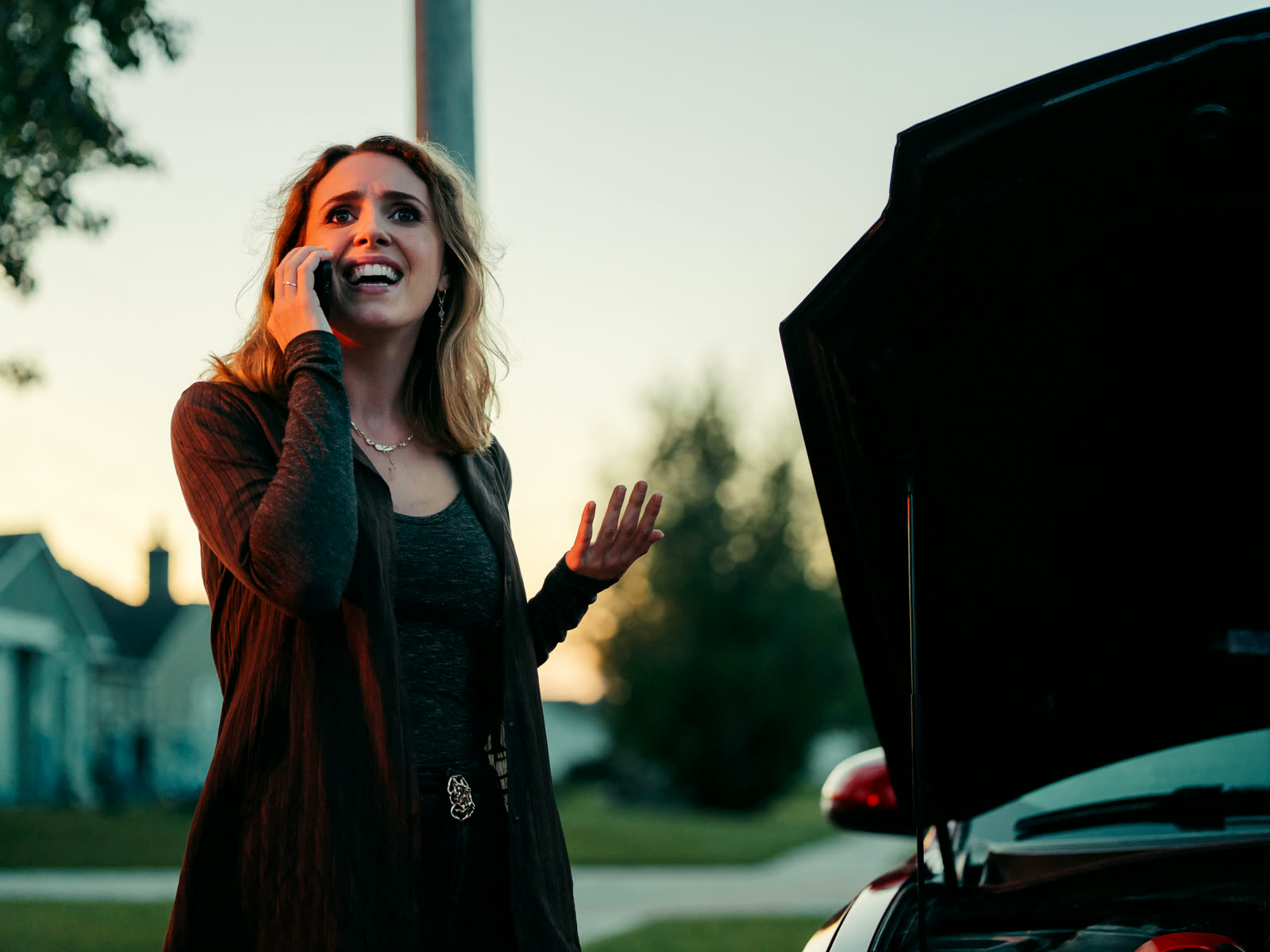 A driver beside her car at dusk looks relieved as her call gets answered and a drop-off gets booked.