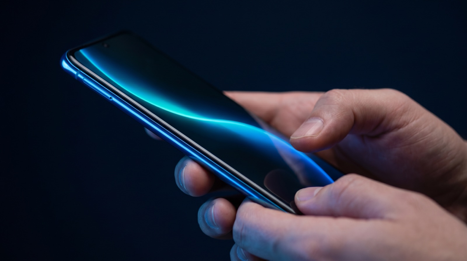 Two hands holding a phone in the dark, the screen glowing with a cyan-blue voice waveform.