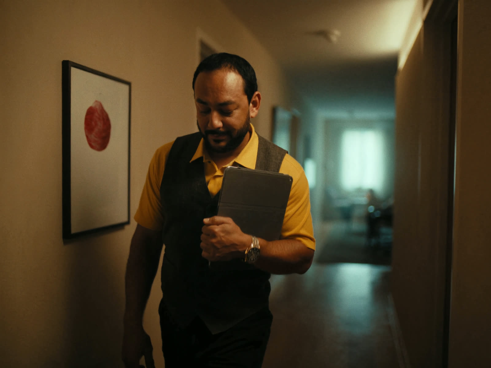 A property manager walks an apartment hallway with a tablet, calm and unhurried.
