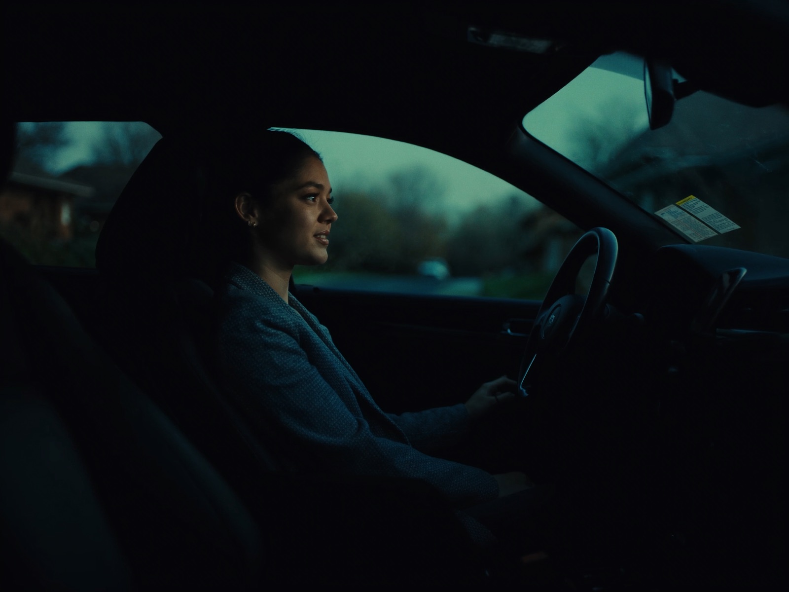 A real estate agent sits calmly in her parked car at dusk between showings on a quiet suburban street.